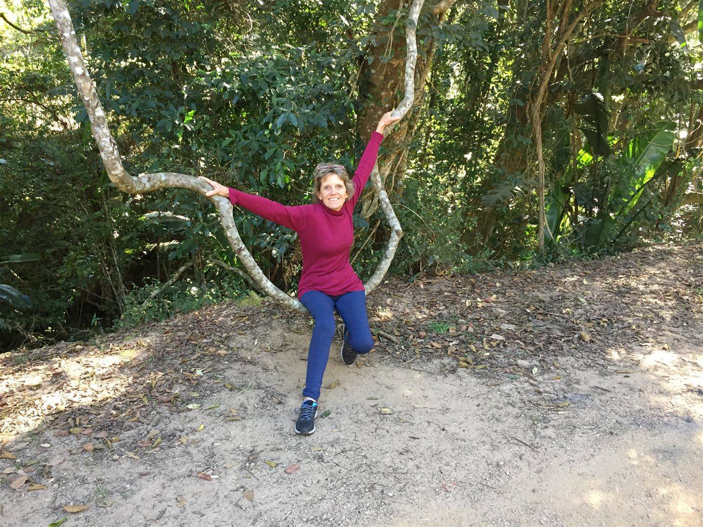 Sue in the forest, arms wide, holding two twisting vines
