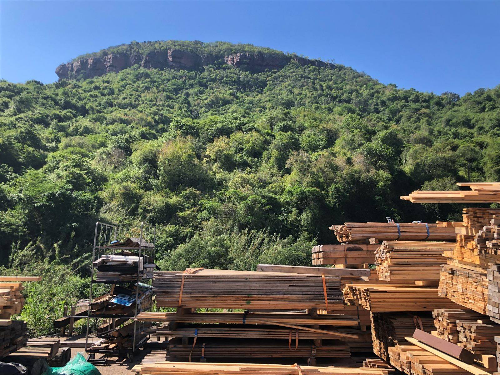 Piles of weathered reclaimed timber in the woodyard, the mountain behind